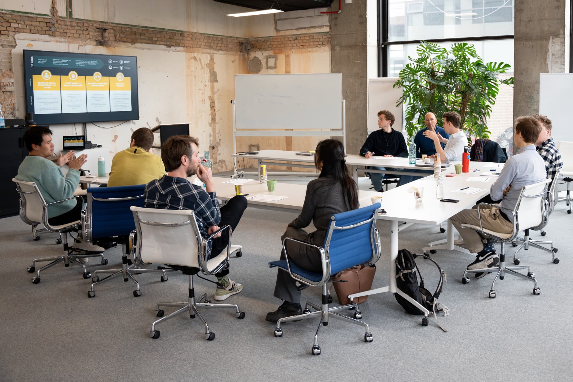 A group of people seated around a table in a bright workshop space, talking and exchanging ideas